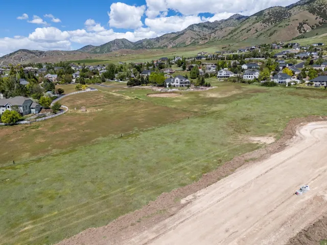 Expansive undeveloped land with a graded dirt road, bordered by established residences and a mountainous backdrop