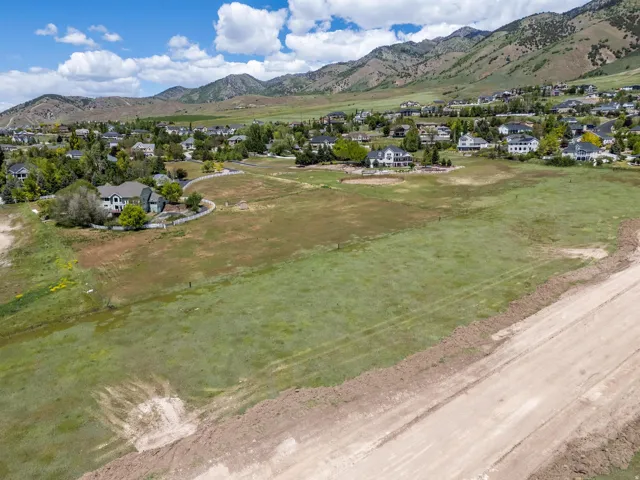 Expansive open land with a partial dirt road, surrounded by established residential properties and distant mountains