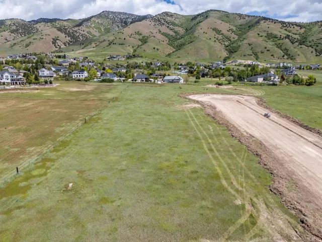 Expansive open land with a partial dirt road, surrounded by distant residential structures and a prominent mountain range backdrop