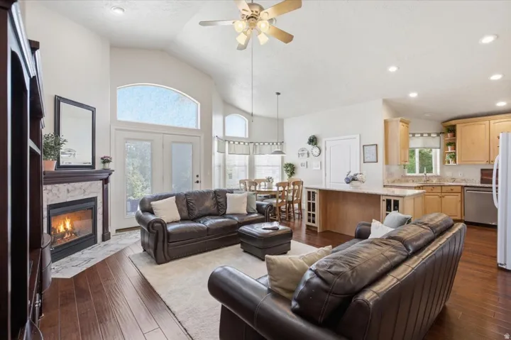 Vaulted ceiling with a ceiling fan, fireplace with a stone surround and wood mantel, wood-finish flooring, and light wood cabinetry with a light-toned countertop