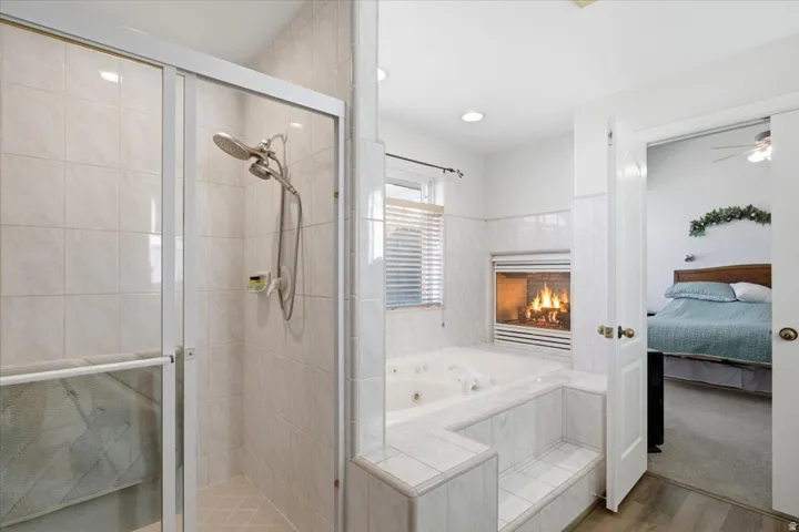 Tiled walk-in shower with glass enclosure, jetted tub with tiled surround, and integrated fireplace