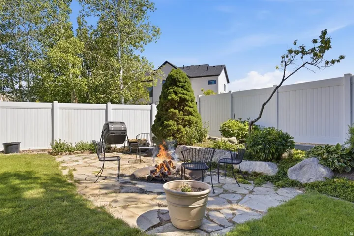 Grassed yard featuring a flagstone patio, fire pit, and white panel fencing