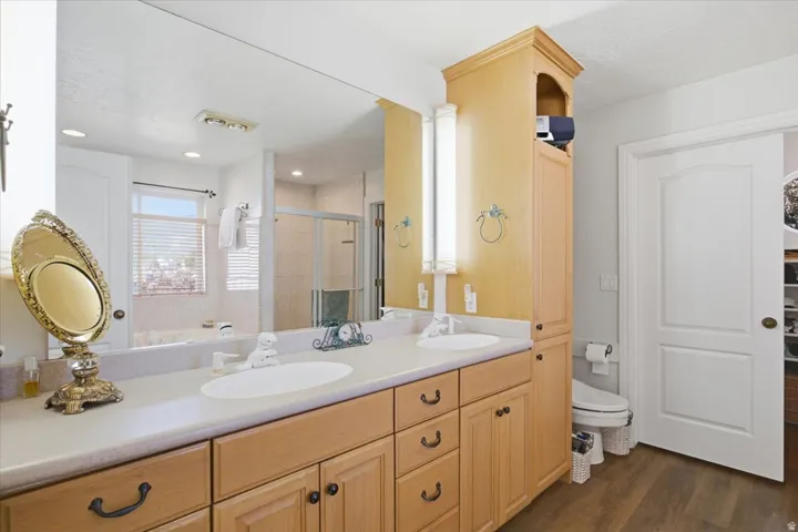 Dual vanity with integrated sinks, wood-finish cabinetry, built-in storage tower, full-width mirror, and wood-finish flooring