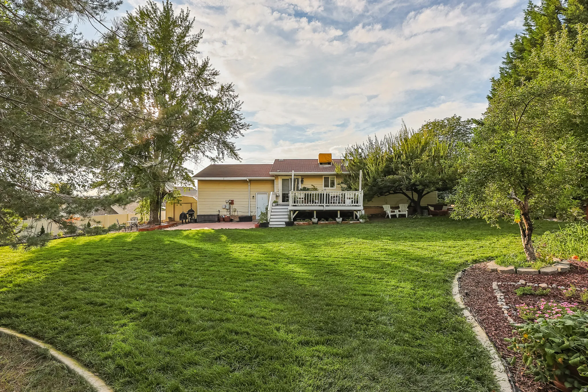 Expansive backyard featuring a manicured lawn, established trees, a multi-level deck, and a patio area