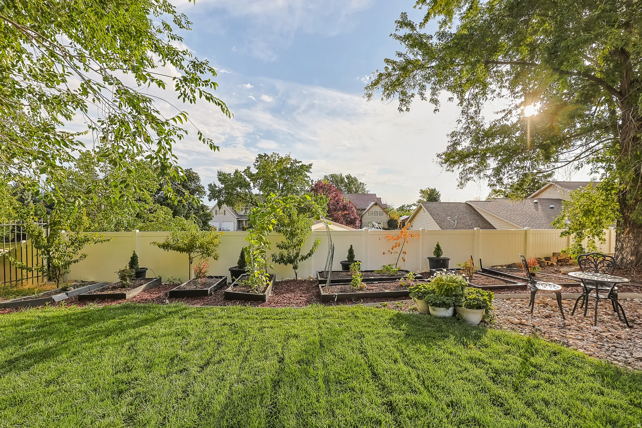 Manicured lawn with raised garden beds, surrounded by a privacy fence, and mature trees providing shade