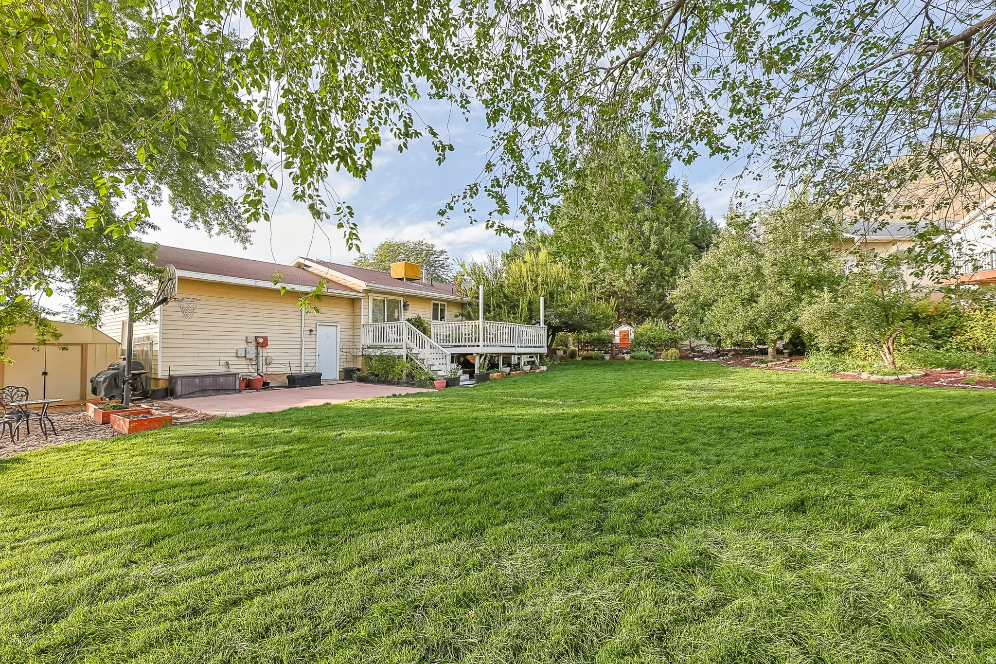 Expansive backyard featuring a manicured lawn, a raised wood deck, a paved patio, and mature trees