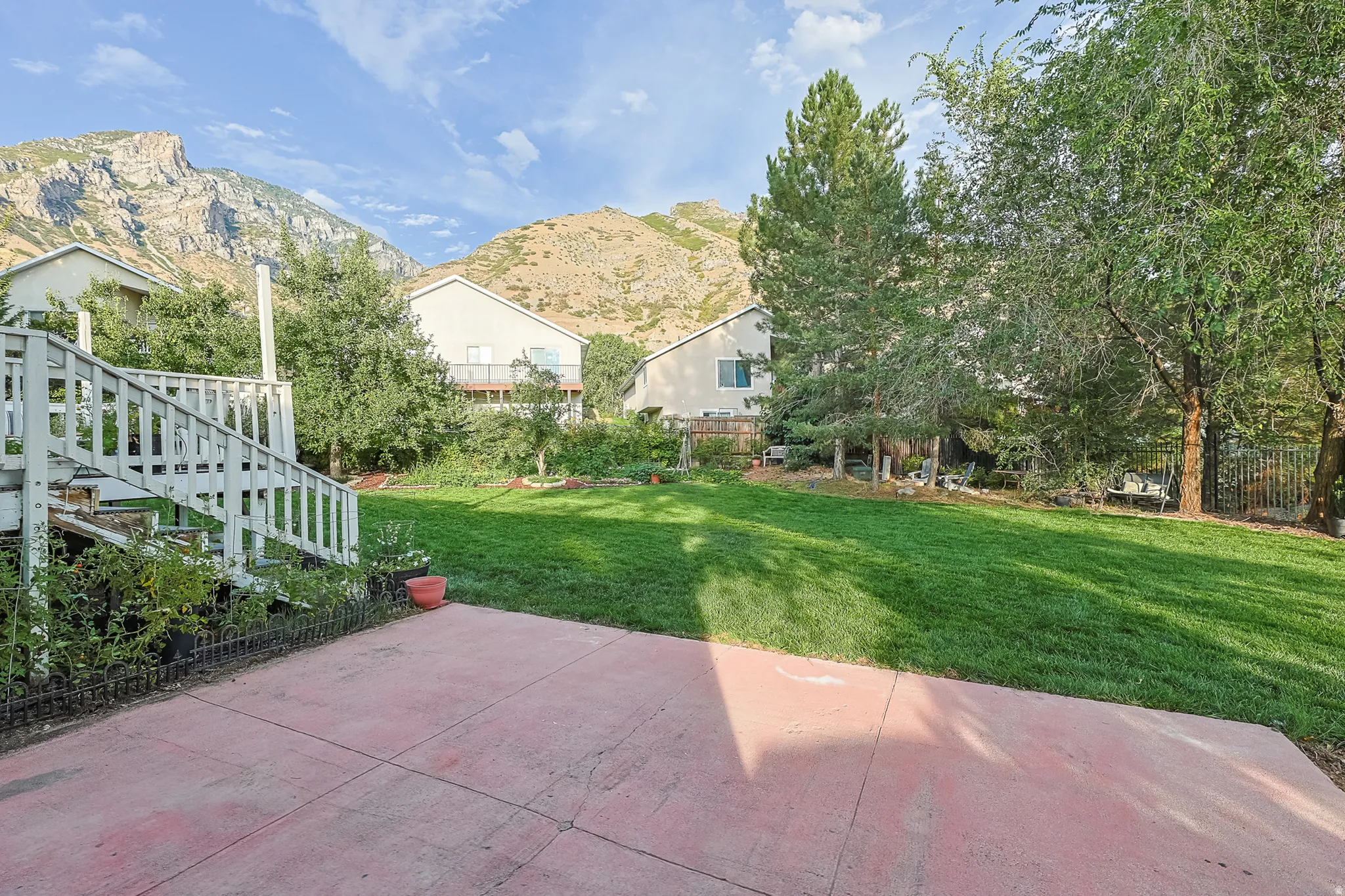 Expansive green lawn with mature trees, concrete patio, and mountain backdrop