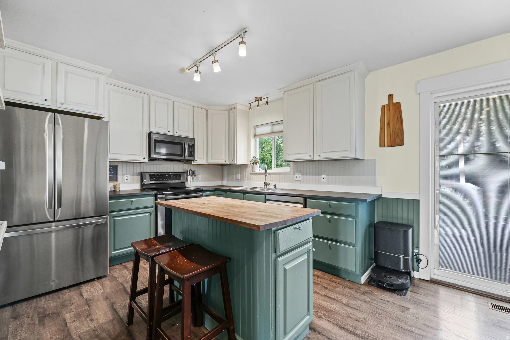Kitchen featuring stainless steel appliances, a central island with a wood countertop, beadboard wainscoting, and a sliding glass door to the backyard