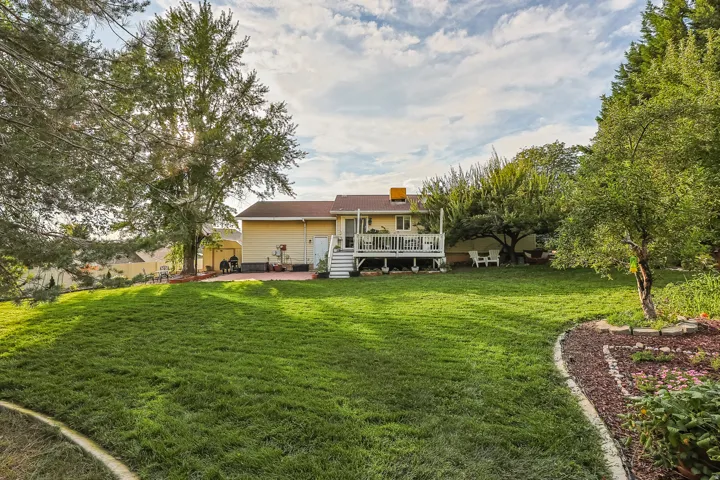 Expansive backyard featuring a manicured lawn, established trees, a multi-level deck, and a patio area