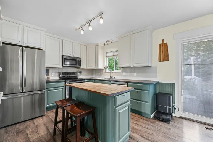 Kitchen featuring stainless steel appliances, a central island with a wood countertop, beadboard wainscoting, and a sliding glass door to the backyard