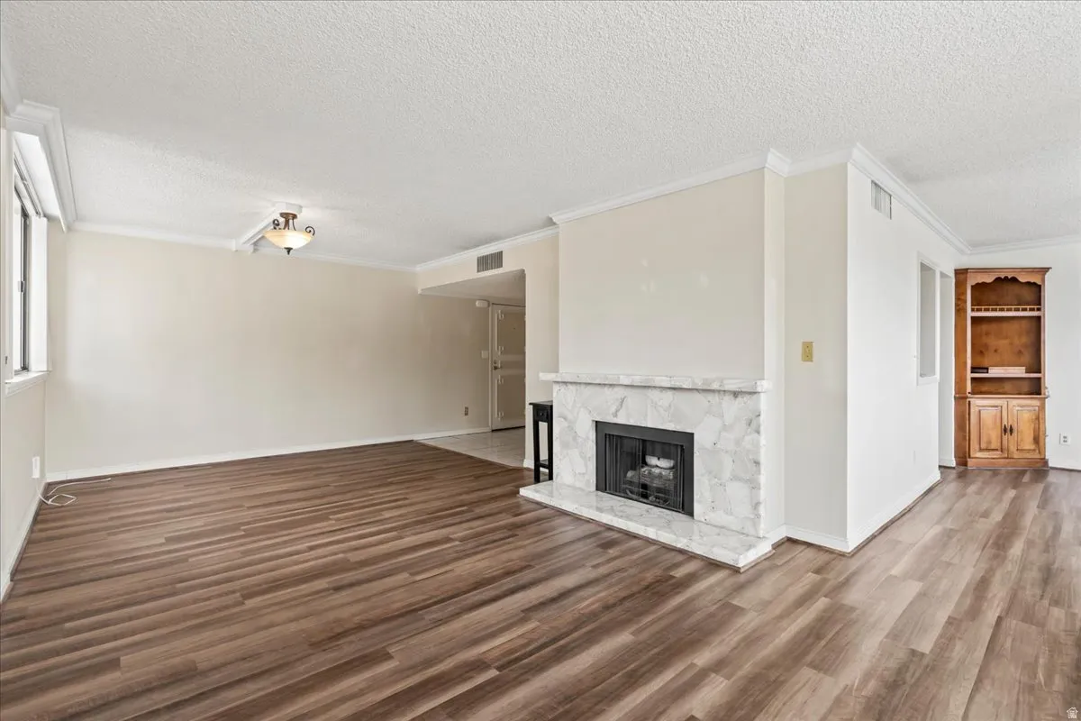 Wood-finish flooring, white crown molding, built-in fireplace with a stone surround, and an integrated wood cabinet with shelving