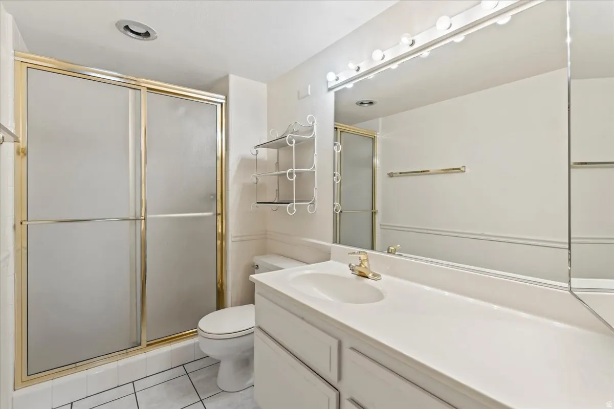 Vanity with integrated sink, gold-finish fixtures, full-width mirror with overhead lighting, and a shower enclosure with gold-finish framing