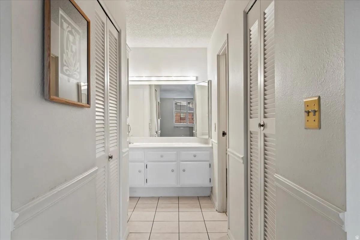 Hallway with white louvered closet doors and tile flooring
