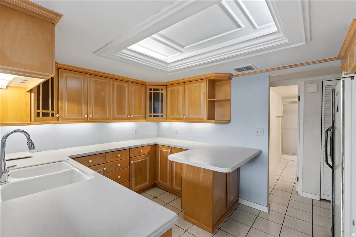 Kitchen featuring wood cabinetry, white countertops, a single basin sink with a gooseneck faucet, and tile flooring