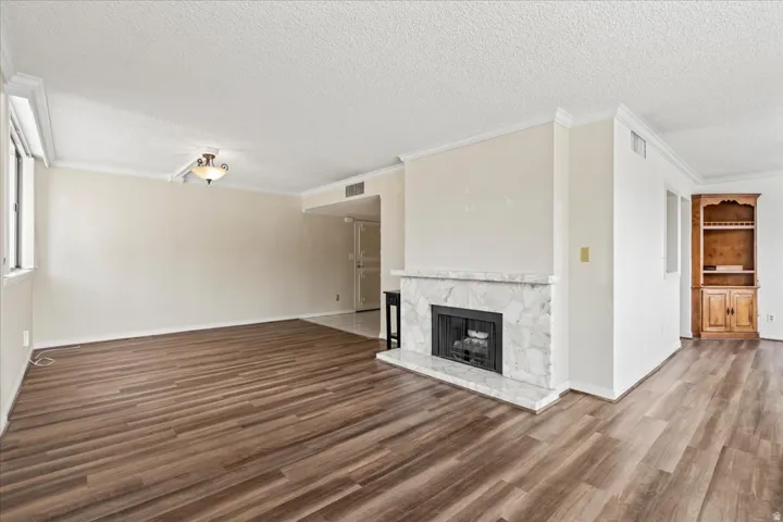 Wood-finish flooring, white crown molding, built-in fireplace with a stone surround, and an integrated wood cabinet with shelving