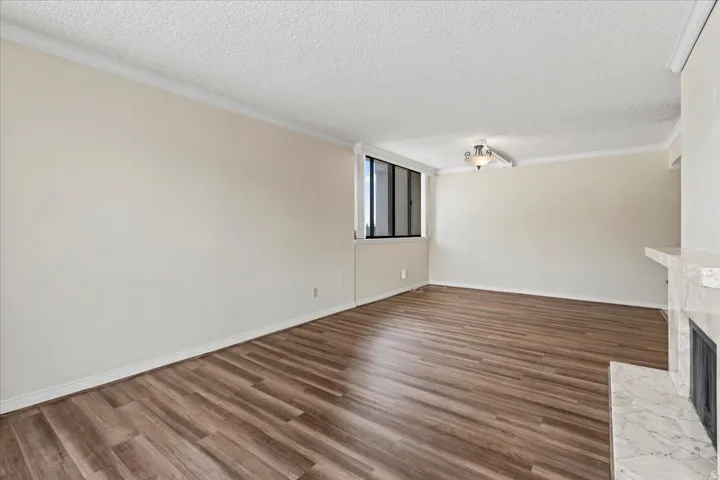 Wood-finish flooring, crown molding, a built-in fireplace with a stone surround, recessed window, and ceiling-mounted light fixture