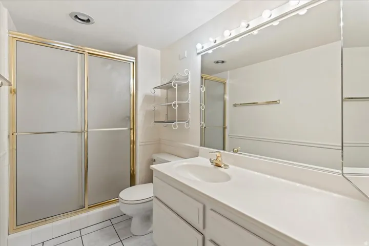 Vanity with integrated sink, gold-finish fixtures, full-width mirror with overhead lighting, and a shower enclosure with gold-finish framing