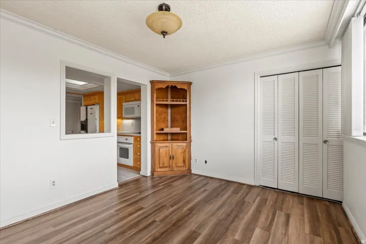 Wood-finish flooring, white walls, crown molding, built-in corner cabinet, and white louvered bi-fold closet doors