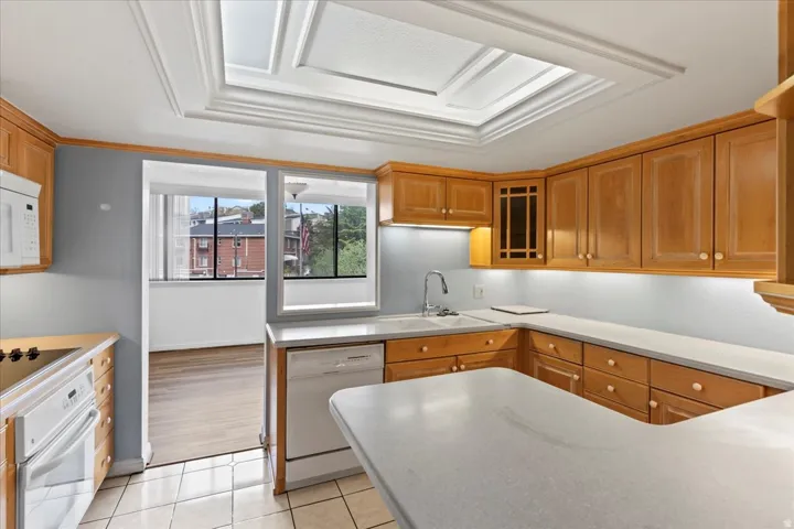 Kitchen featuring a coffered ceiling with a skylight, wood cabinetry, light-toned countertops, and a white dishwasher