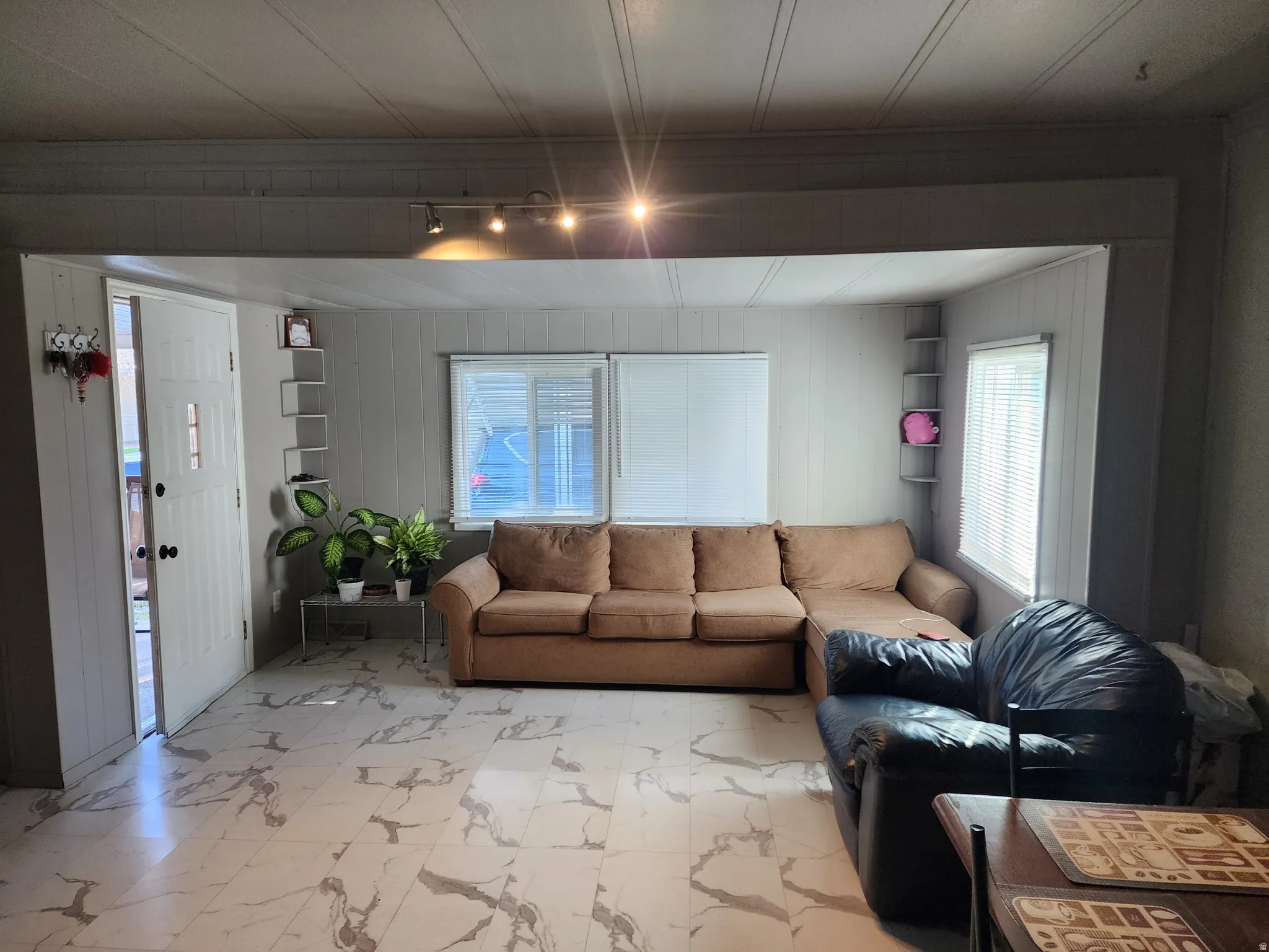 White-paneled entry door, track lighting, two windows with blinds, built-in shelving, and white-and-gray patterned flooring