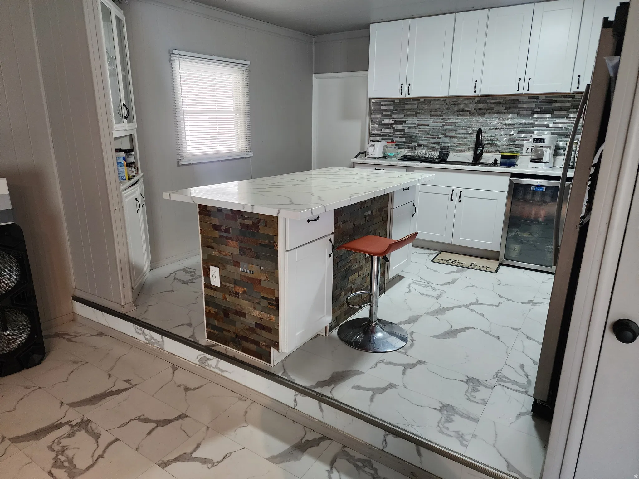 Kitchen featuring white cabinetry, large center island with stone veneer detailing, stone-finish countertop, and tile backsplash