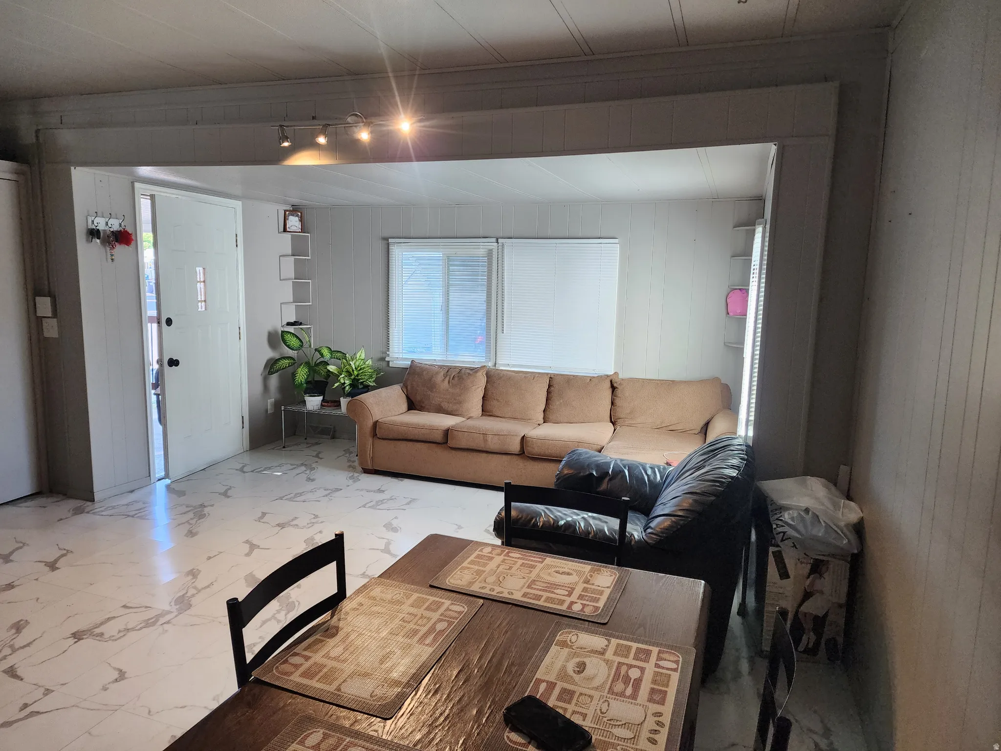 Open-concept living space with track lighting, white paneled walls, and white-patterned flooring
