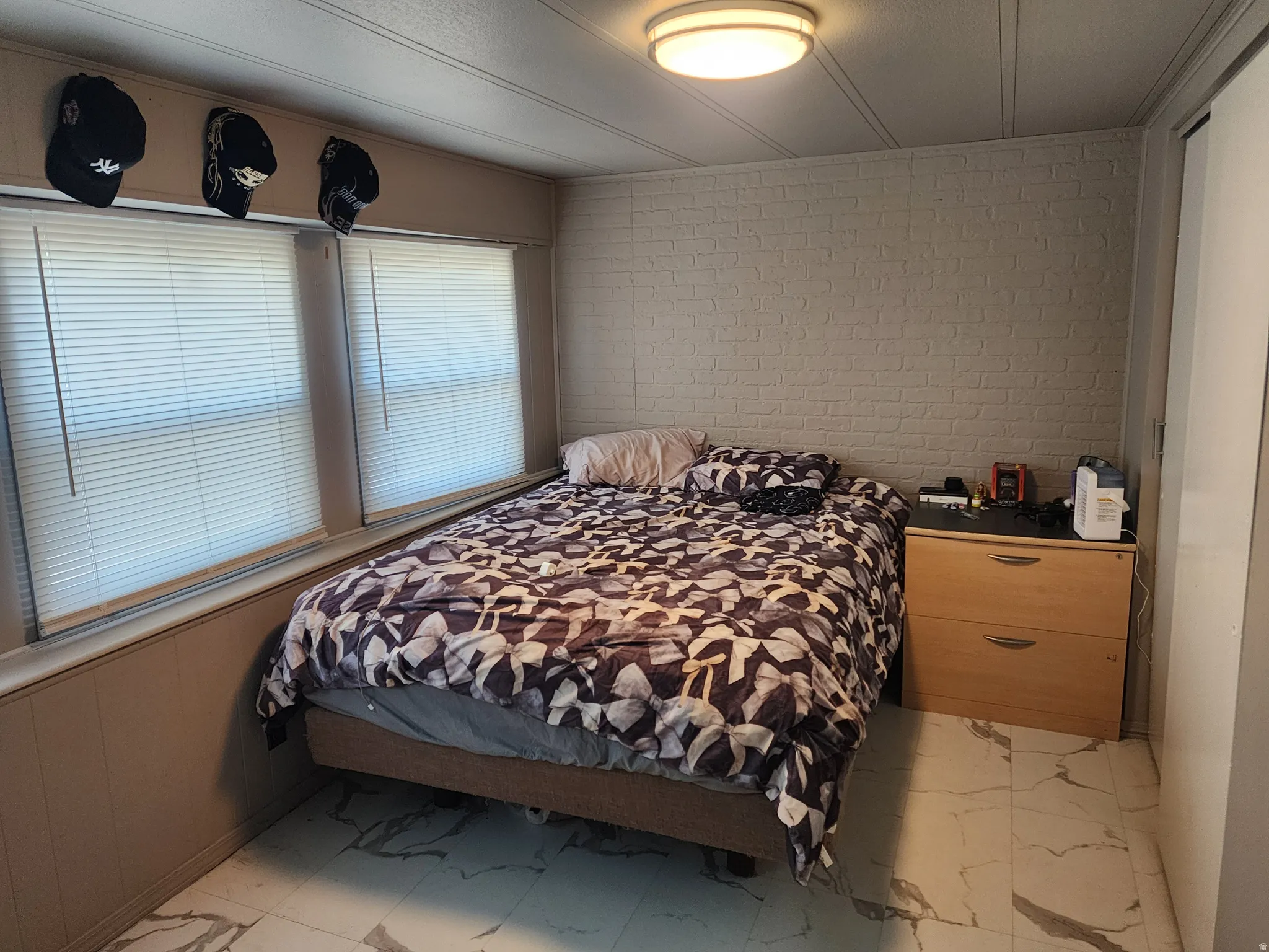Two windows with blinds, wood-finish paneling, an accent wall with brick-patterned wallpaper, and ceiling-mounted lighting