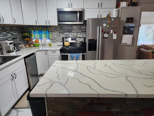 Kitchen featuring white cabinetry, stainless steel appliances, a tile backsplash, light-toned countertops, and an integrated beverage cooler