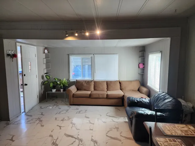 White-paneled entry door, track lighting, two windows with blinds, built-in shelving, and white-and-gray patterned flooring