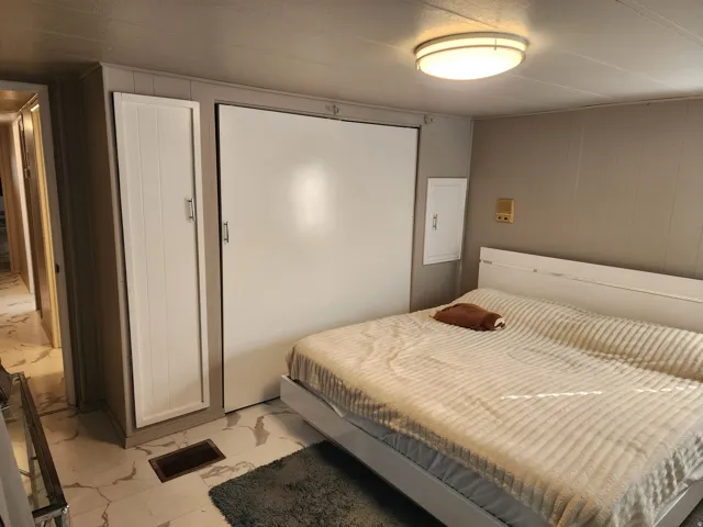 Recessed ceiling lighting illuminates a room featuring a built-in cabinet and a wall-mounted panel