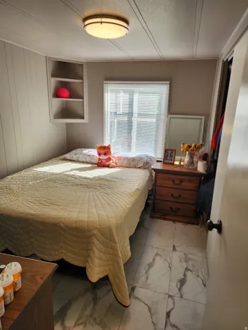 White paneling, built-in shelving, window with blinds, wood-finish flooring, and a flush mount ceiling light