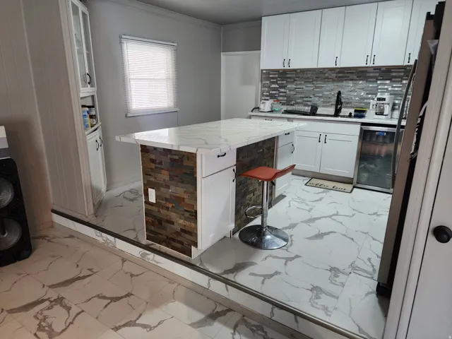Kitchen featuring white cabinetry, large center island with stone veneer detailing, stone-finish countertop, and tile backsplash