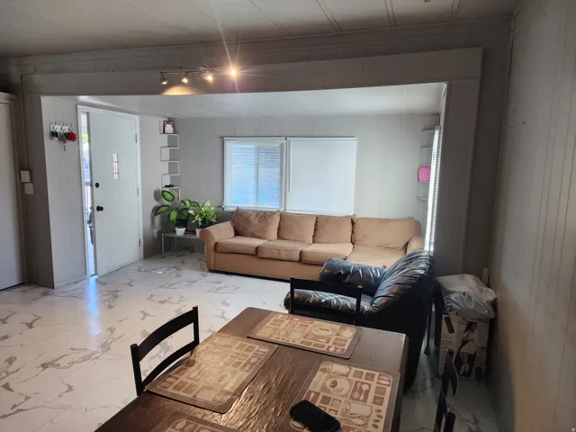 Open-concept living space with track lighting, white paneled walls, and white-patterned flooring
