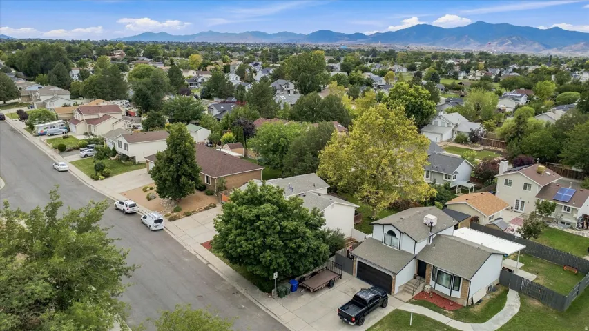 Aerial view showcasing a well-appointed residence on a generous lot with mature landscaping, situated in an established neighborhood with mountain vistas in the distance