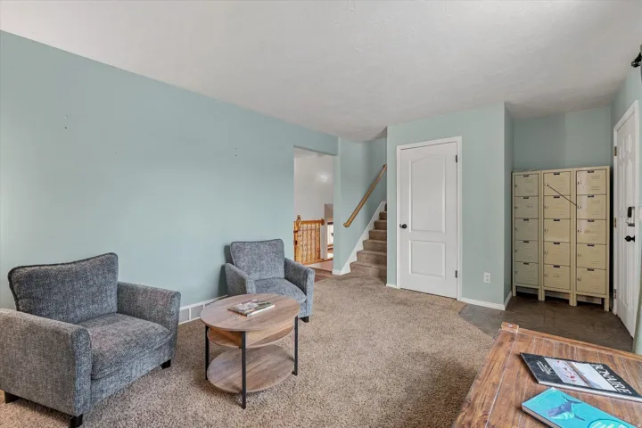 Spacious open-concept living area featuring soft blue-green walls, neutral carpeting, and abundant natural light