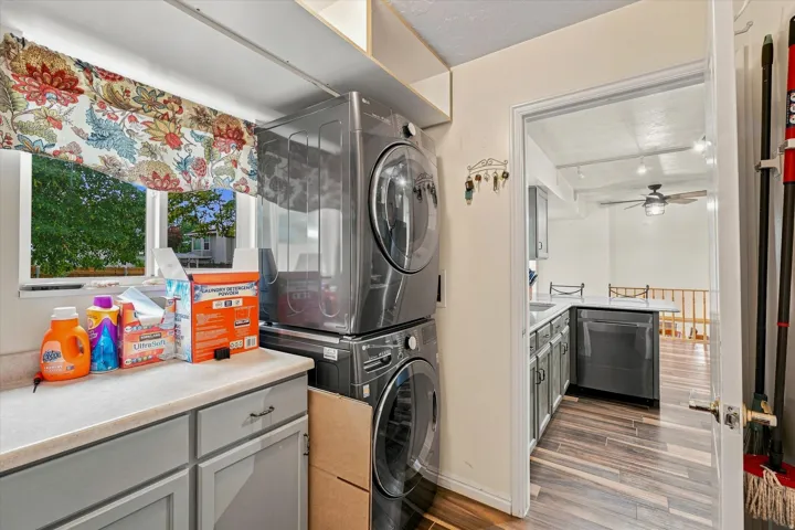 Efficient laundry room featuring stacked washer and dryer units, white cabinetry with wood-finish countertop, and direct access to adjacent spaces