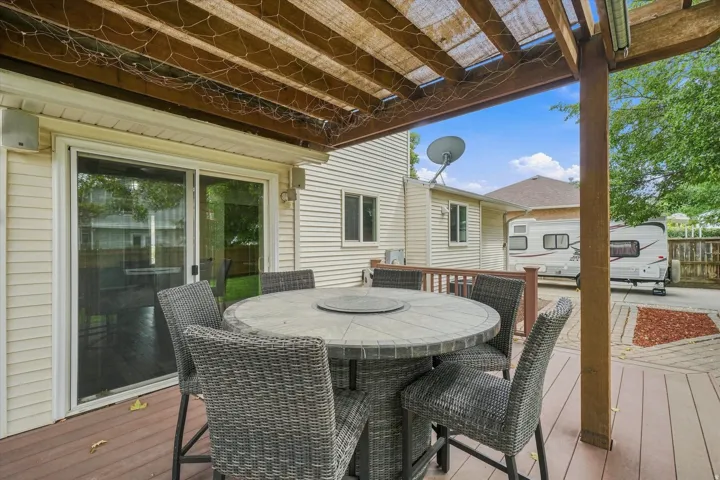 Covered deck featuring a wood-finish pergola with integrated skylights, round stone-top dining table, and wicker seating