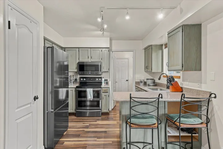 Modern kitchen featuring stainless steel appliances, white cabinetry with wood-tone accents, wood-finish flooring, granite countertops, and a breakfast bar with seating for two