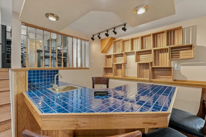 Custom-built wet bar featuring a blue tile countertop with wood-finish cabinetry, recessed lighting, and extensive built-in shelving with glass-front display cases