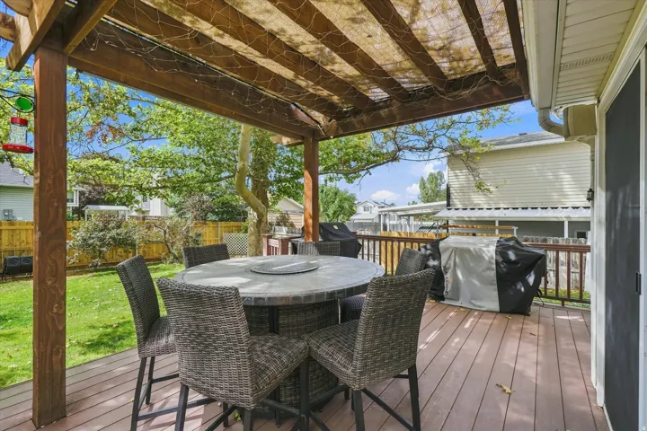 Expansive composite deck featuring a wood-finish surface, pergola with lattice overhead, and integrated dining area with stone-top table
