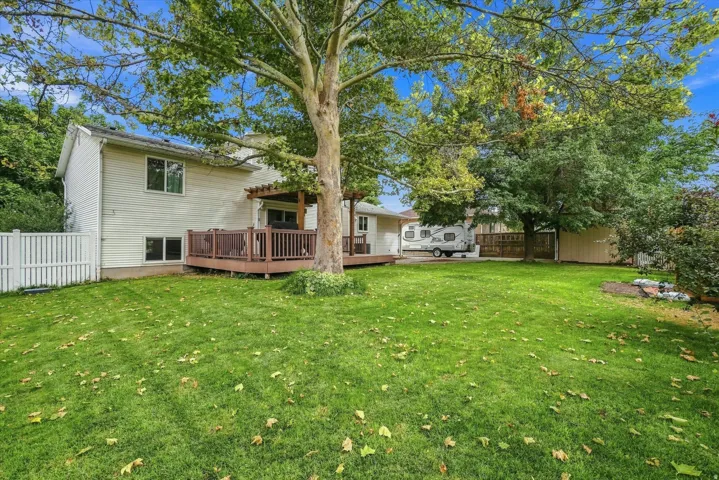 Spacious backyard with mature shade trees and lush lawn, complemented by a multi-level home featuring a wood deck, siding exterior, and established landscaping throughout the grounds