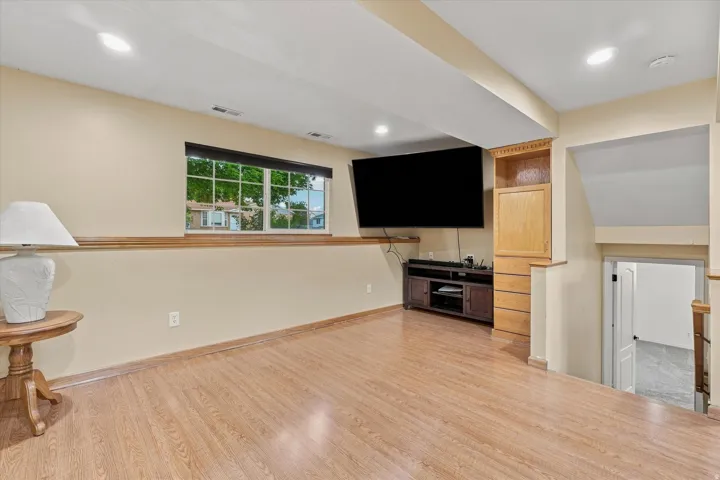 Spacious recreation room featuring gleaming wood-finish flooring, recessed lighting, and a wall-mounted flat-screen television