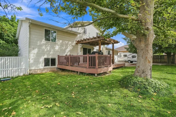 Spacious backyard oasis featuring a mature shade tree, manicured lawn, and a wooden deck with pergola structure