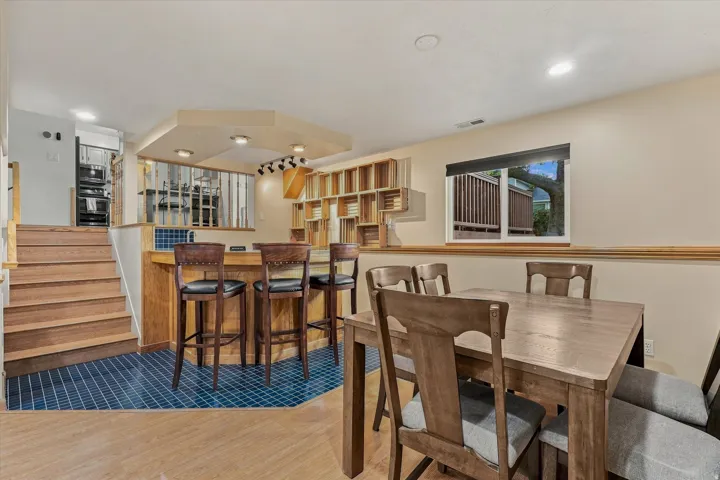 Open-concept entertaining space featuring wood-finish flooring, a dining table with seating for six, and a bar-height counter with three stools