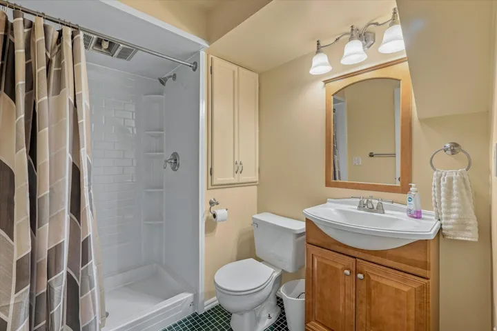 Spa-inspired bathroom featuring a walk-in shower with subway tile surround, wood-finish vanity with dual-handle faucet, arched mirror with wood frame, and ceramic tile flooring