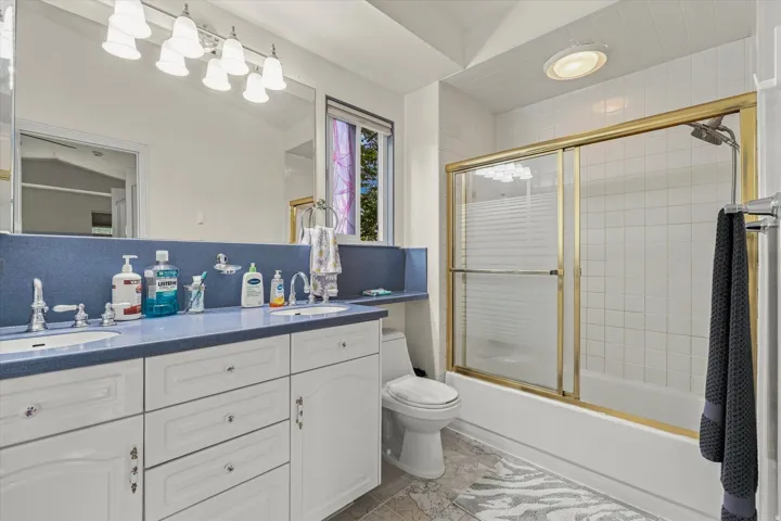 Spa-inspired bathroom featuring a dual vanity with white cabinetry and blue tile backsplash, framed mirror with brass accents, and a walk-in shower with subway tile surround and brass fixtures