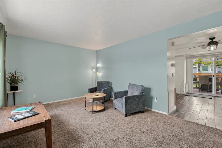 Spacious living room with soft blue walls, neutral carpeting, and abundant natural light from glass doors opening to an outdoor patio area