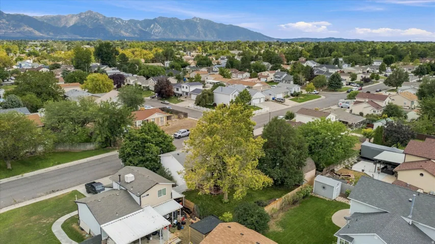 Aerial perspective showcasing this residential property situated on a generous lot with mature landscaping, tree-lined grounds, and mountain backdrop