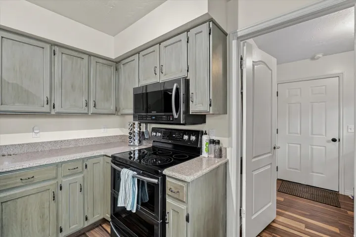 Updated kitchen featuring light wood-finish cabinetry with brushed metal hardware, quartz countertops, black stainless steel appliances including a gas range and microwave, and neutral subway tile backsplash
