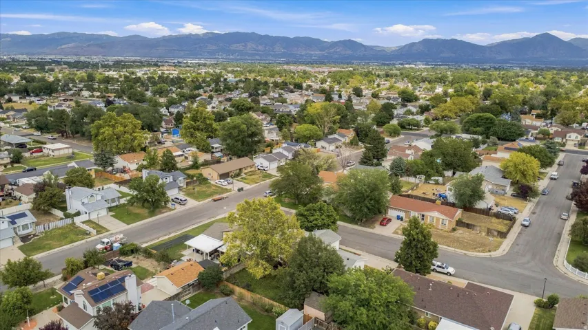 Aerial perspective showcasing a tree-lined residential neighborhood with mature landscaping, curved street design, and single-family homes situated on spacious lots against a backdrop of distant mountain ranges